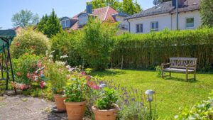 Blühender Sommergarten des Grundstücks in Forstenried mit Sitzbank vor grüner Hecke