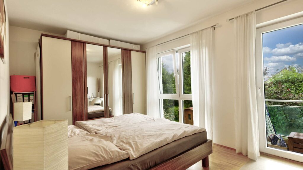 Bedroom with a double bed, wardrobe, and access to the balcony in Munich-Forstenried