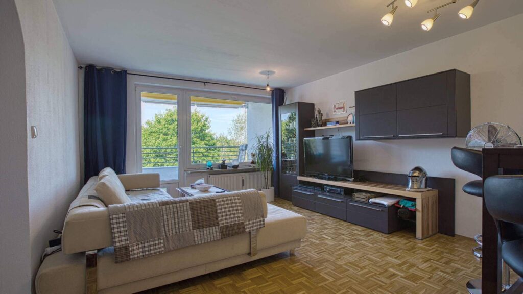 Lived-in living room with a bright couch, wall unit, parquet flooring, and a large window in an apartment in Forstenried.