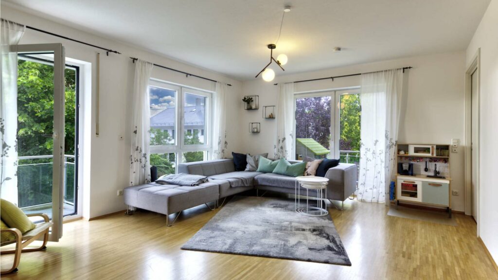 Bright living room with a corner sofa, parquet flooring, and two balcony accesses in Munich-Forstenried