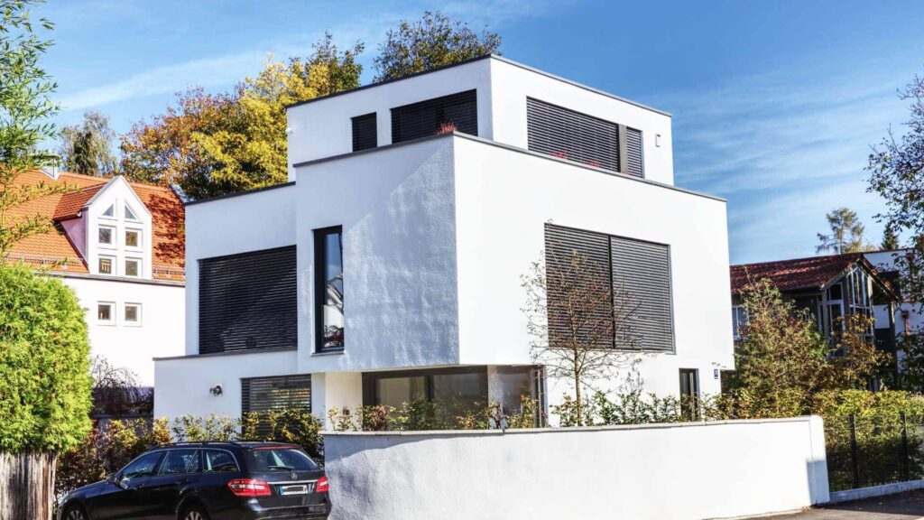 Modernes weißes Kubushaus mit großen Fenstern und begrüntem Vorgarten – Symbolbild zu häufigen Fragen von Immobilienkäufern