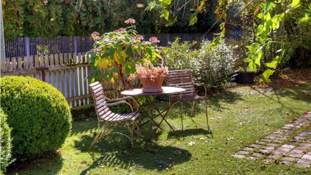 Kleiner Sitzplatz mit Tisch und Stühlen zwischen Buchsbaum und Rosen im Garten