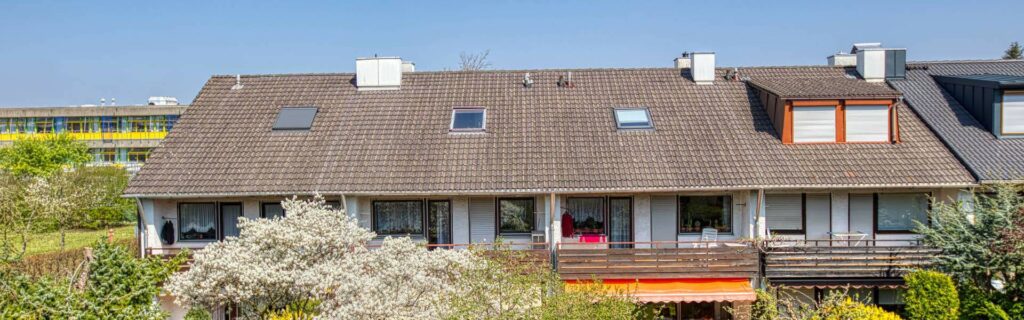 Panoramic view from the balcony of a townhouse development with blooming shrubs and a blue sky in Germering.