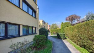 Exterior view of an apartment building with a well-maintained path, hedges, and a blue sky in Germering.