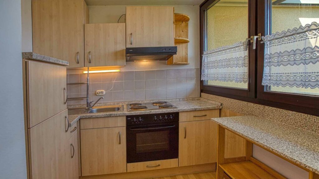 Compact fitted kitchen with wooden fronts, stove, and window seating area with a view in an apartment in Germering.
