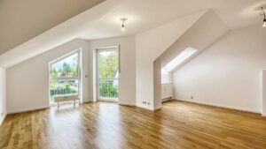Leeres Wohnzimmer mit Dachschräge, Parkettboden und großen Fenstern zum Balkon in einer Wohnung in Germering.