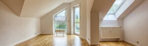 Leerer Wohnbereich mit Dachschräge, Parkettboden und zwei Fenstertüren zum Balkon in Germering.