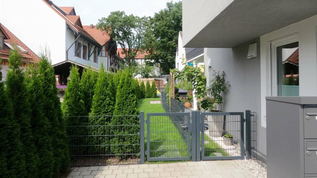 Gepflasterter Gartenweg mit Hecke und Gartentor zum Hauseingang einer Immobilie in Gröbenzell