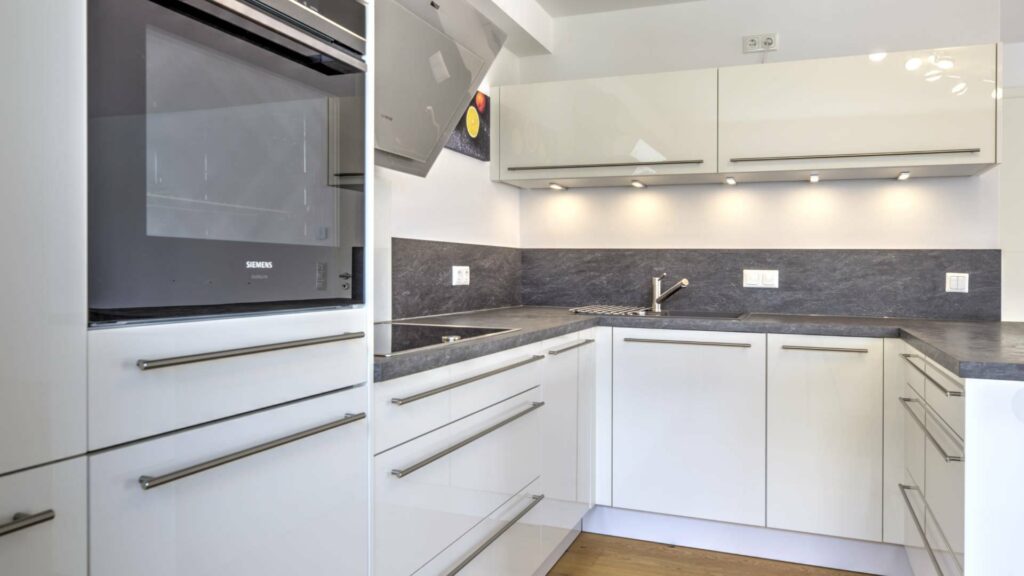 Detailansicht einer weißen Küchenzeile mit dunkler Steinarbeitsplatte, Backofen und Beleuchtung in einer Wohnung in Gröbenzell