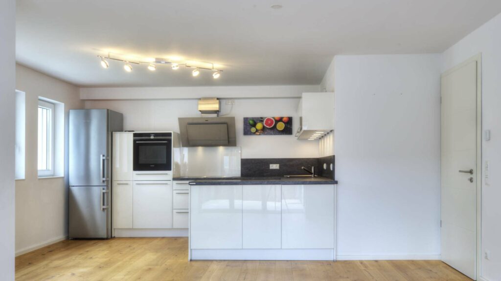 Offene, weiße Einbauküche mit Kühlschrank und angrenzendem Wohnbereich mit Holzboden in einer Wohnung in Gröbenzell