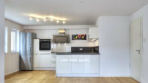 Offene, weiße Einbauküche mit Kühlschrank und angrenzendem Wohnbereich mit Holzboden in einer Wohnung in Gröbenzell