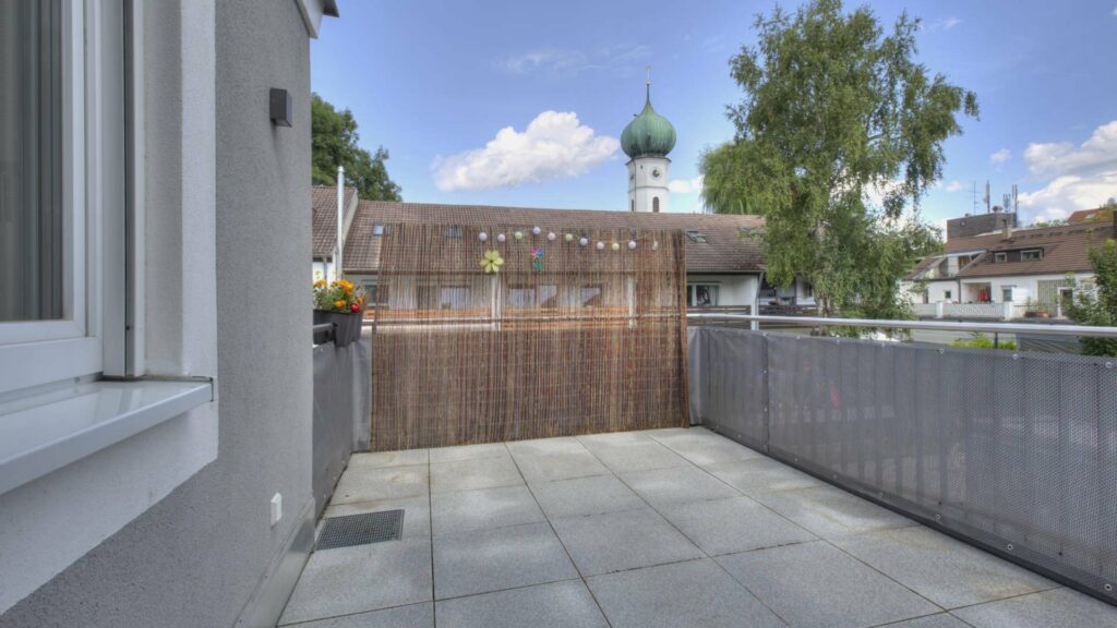 Gefliester Dachterrassenbereich mit Sichtschutz und Blick auf den Kirchturm in Gröbenzell.
