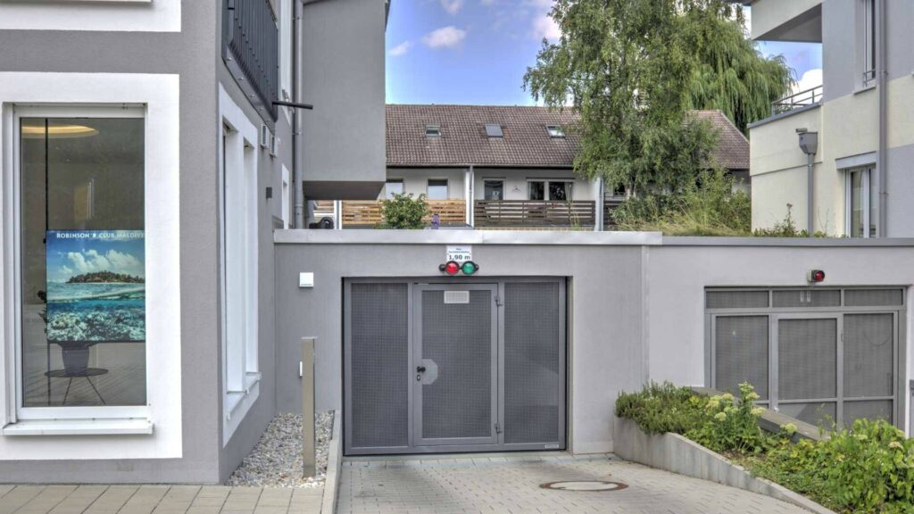 Tiefgarageneinfahrt mit Rolltor und gepflegten Beeten an einem Wohnhaus in Gröbenzell.