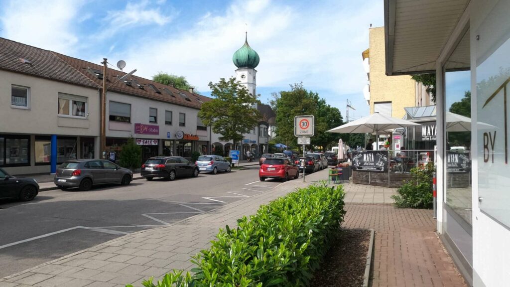 Fußgängerzone mit Geschäften, Zwiebelturm und Straßencafé in der Ortsmitte von Gröbenzell.