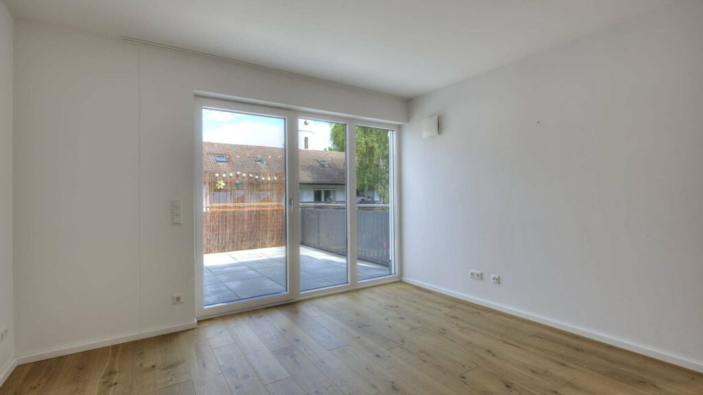 Leeres Wohnzimmer mit Parkettboden und Glastür mit Blick auf Nachbarhäuser in einer Wohnung in Gröbenzell.