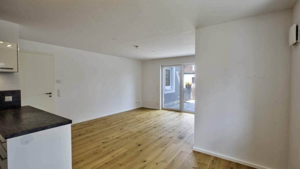 Leerer Wohnbereich mit Küchenzeile, Parkettboden und Terrassentür in einer Wohnung in Gröbenzell.