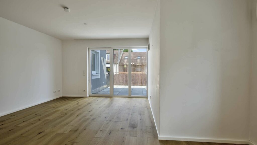 Leeres Wohnzimmer mit Parkettboden und Glastür mit Blick auf die Terrasse in einer Wohnung in Gröbenzell.