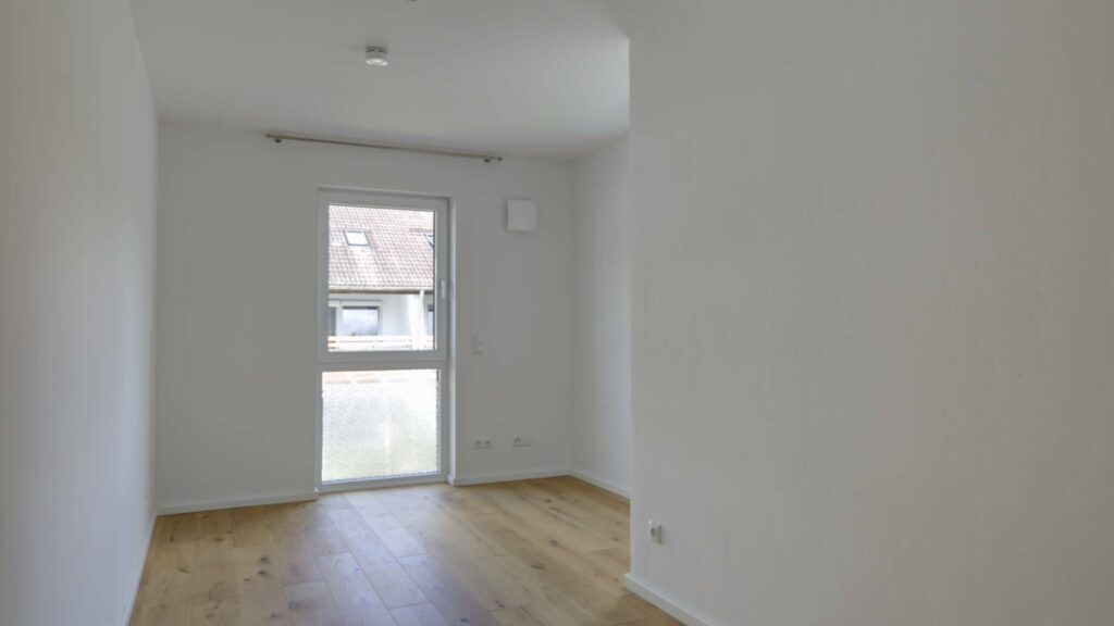 Leeres Zimmer mit Parkettboden, Fenstertür und Balkonzugang in einer neuwertigen Wohnung in Gröbenzell.