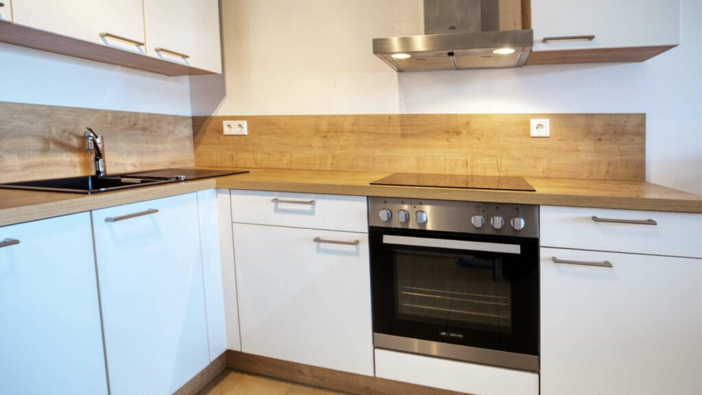 Weiße Einbauküche der Großhadener Wohnung mit Ceranfeld, Backofen und Holzarbeitsplatte