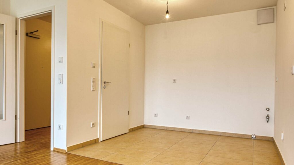 Leeres Zimmer der Großhadener Wohnung mit Fliesenboden und Türdurchgang zum Flur