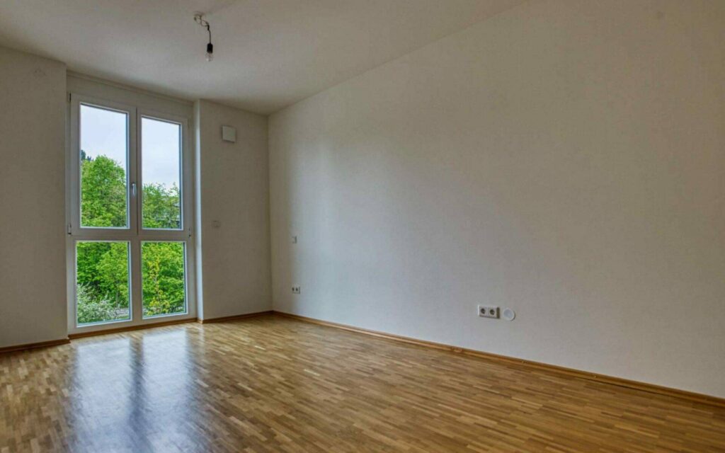 Leeres Schlafzimmer der Großhadener Wohnung mit Parkettboden und Grünblick in Großansicht
