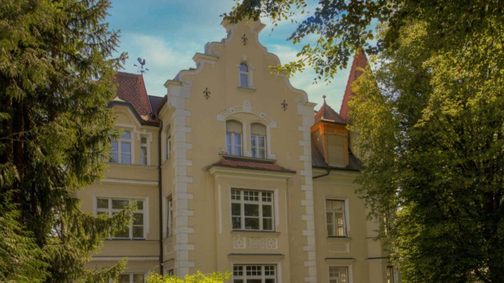 Historischer Gebäudegiebel mit Türmchen zwischen Bäumen in München