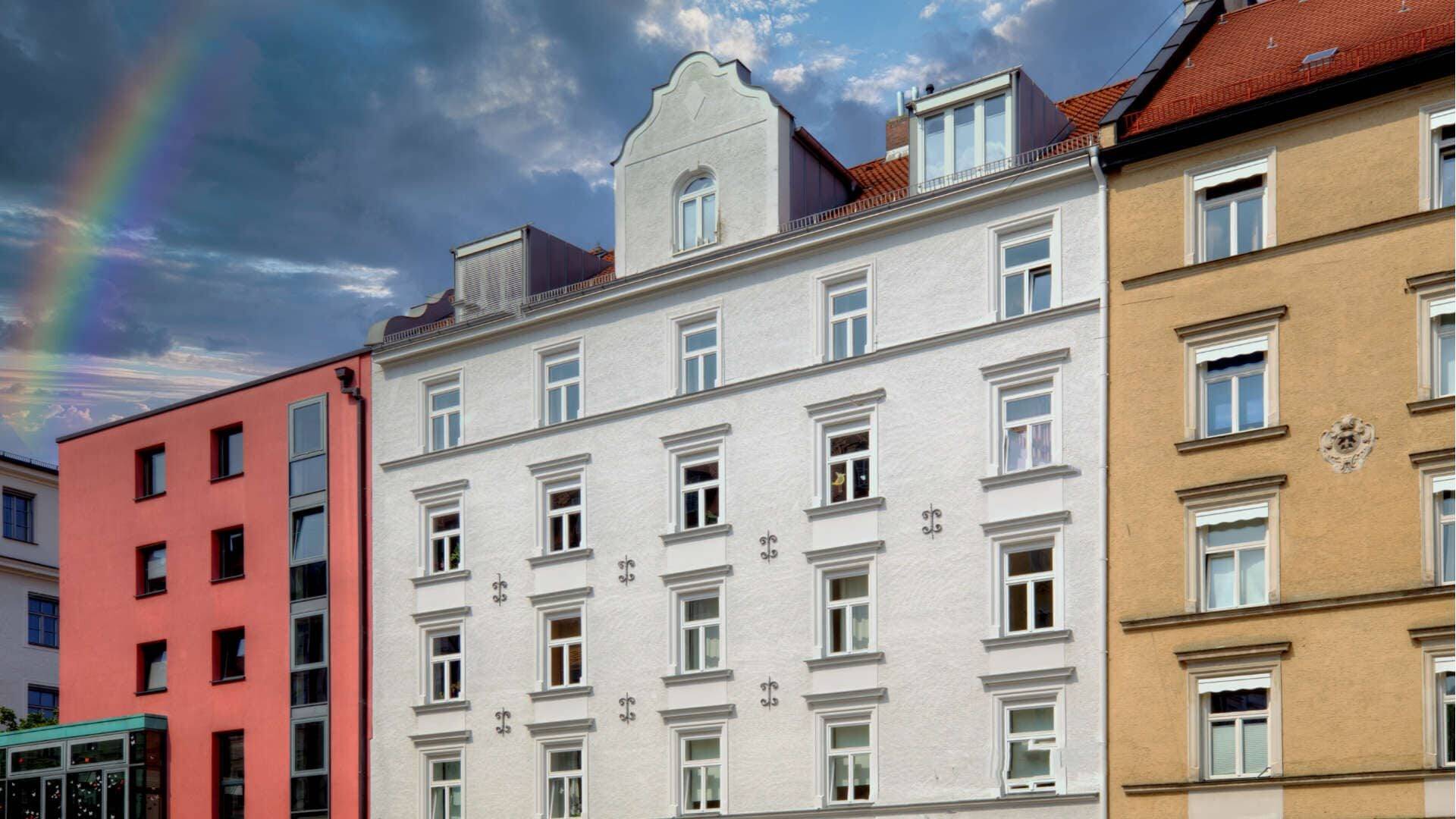 Bunte Altbaufassaden in Rosa, Weiß und Gelb mit Regenbogen am Himmel in München