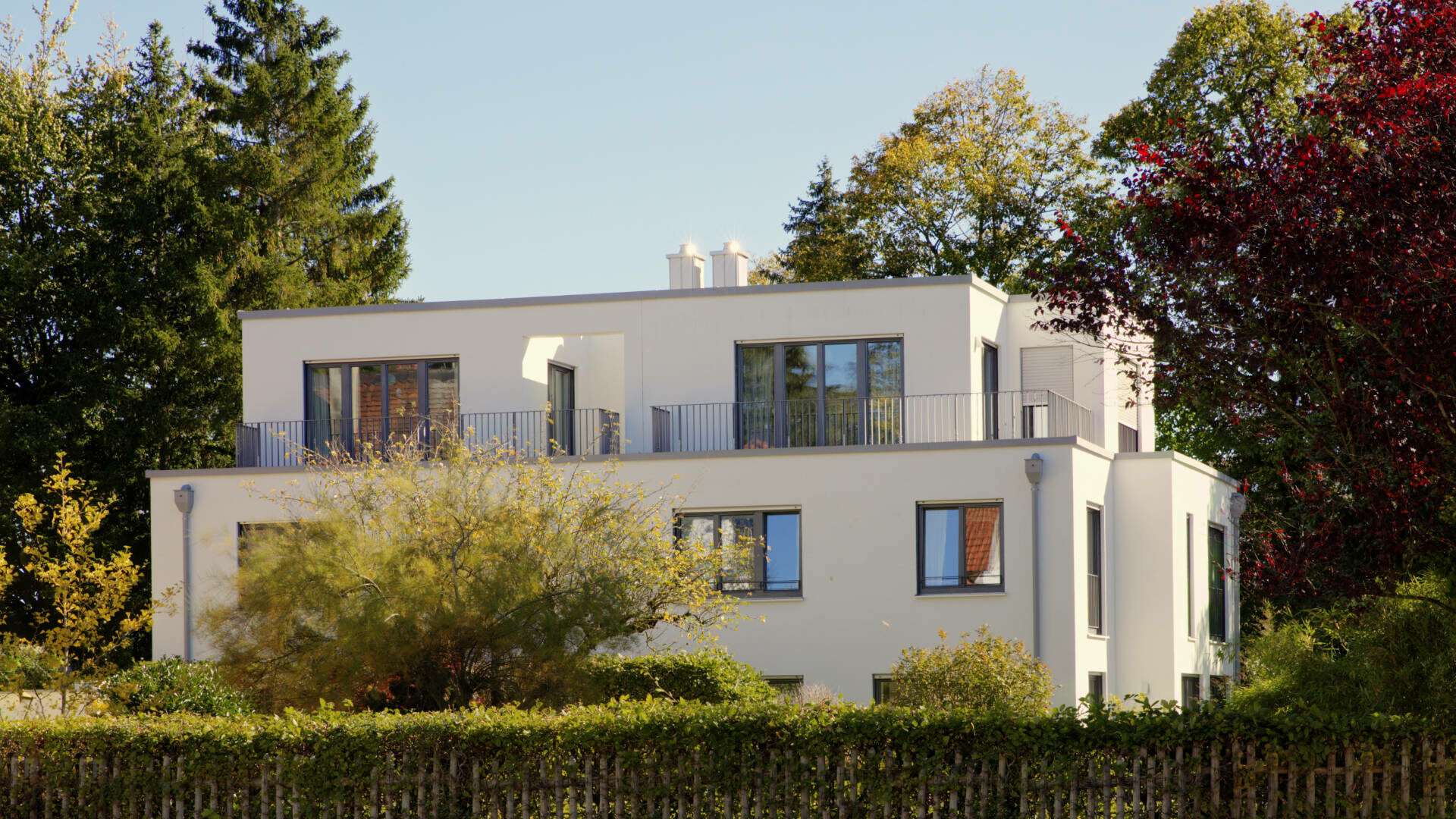 Weiße moderne Villa mit rundem Erker vor buntem Herbstlaub