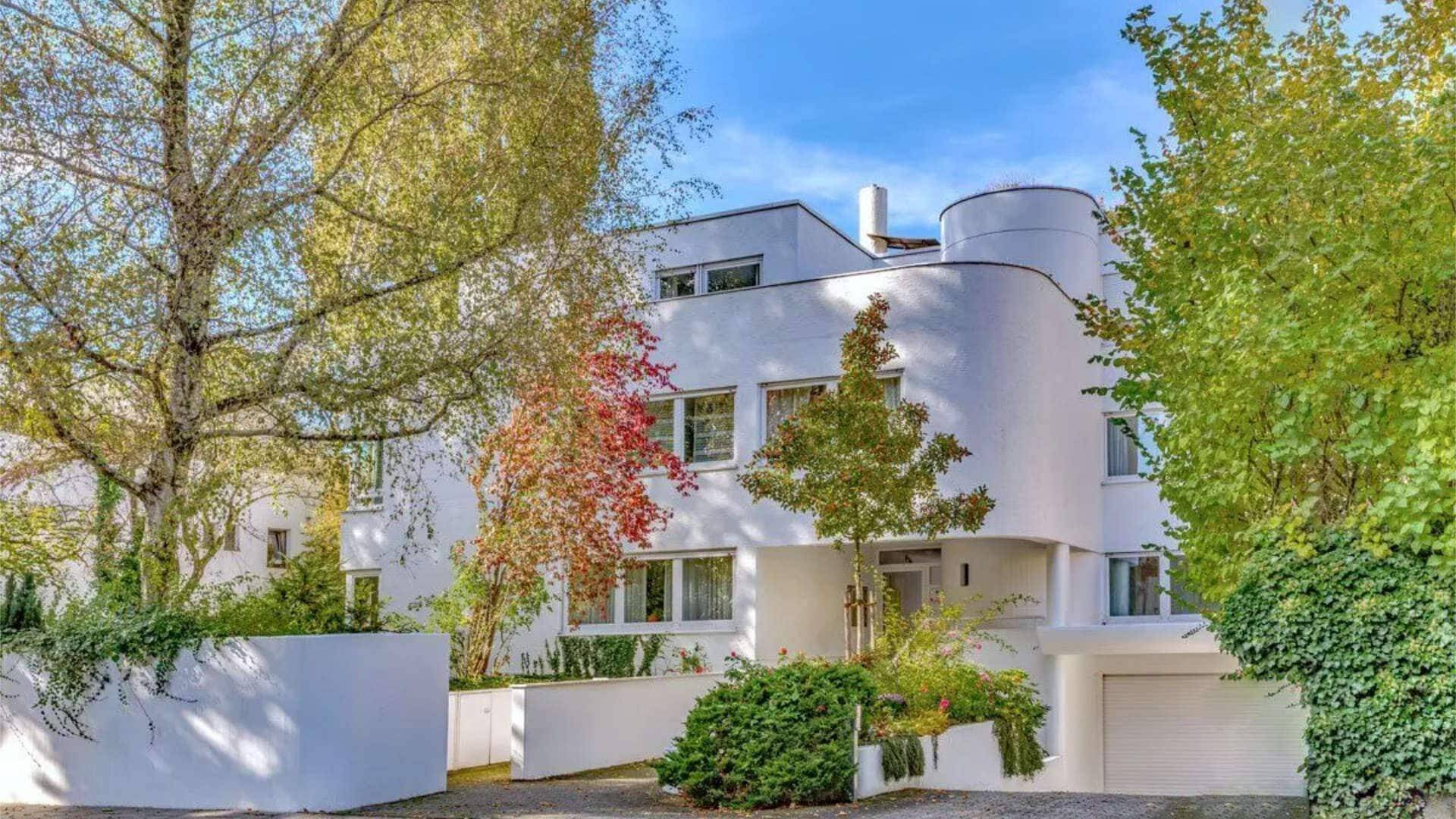 Weiße Villa im Bauhausstil mit runden Erkern und herbstlich gefärbten Bäumen
