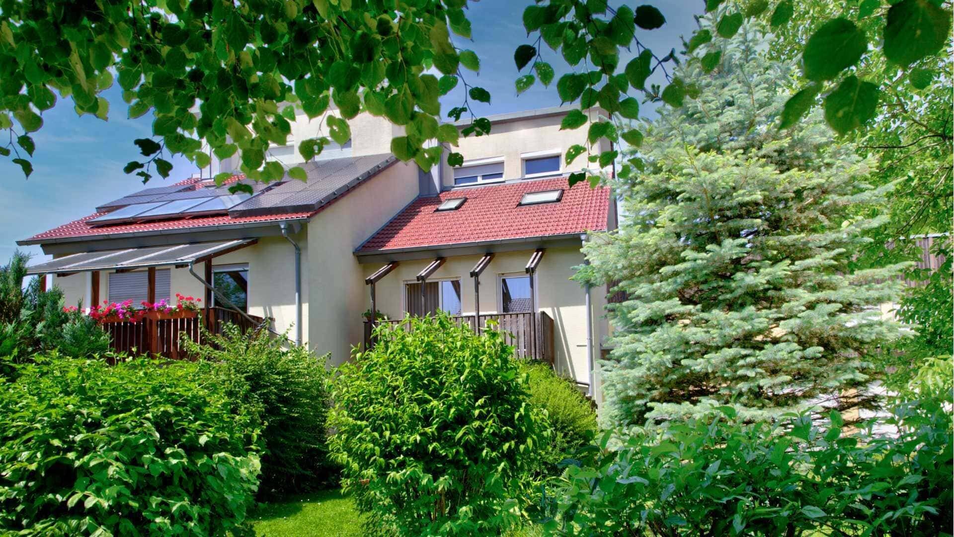 Wohnhaus mit Photovoltaikanlage auf dem Dach hinter dichtem Grün in Puchheim
