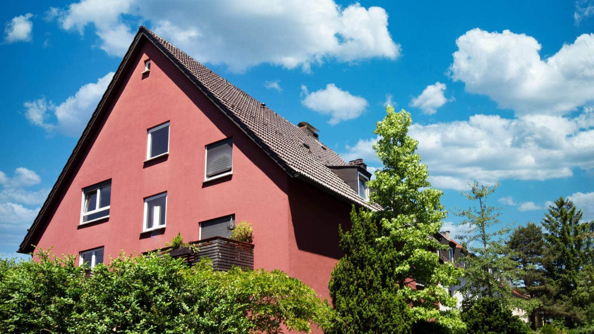 Rotes Giebelhaus mit dunklem Dach hinter dichter Hecke – Symbolbild zu Immobilienpreisen in München-Allach