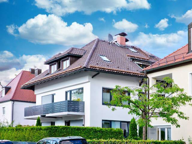 Weißes und cremefarbenes Mehrfamilienhaus mit Balkon und Hecke – Symbolbild zu Immobilienpreisen in Berg am Laim