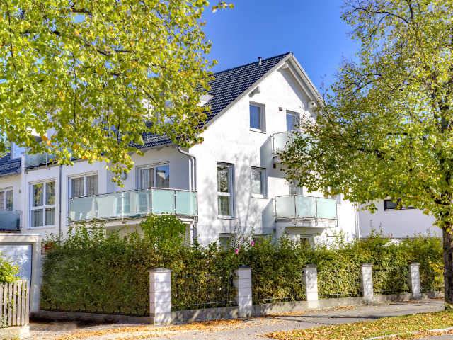 Mehrfamilienhaus mit Glasbalkonen hinter herbstlich gefärbten Bäumen in München-Forstenried