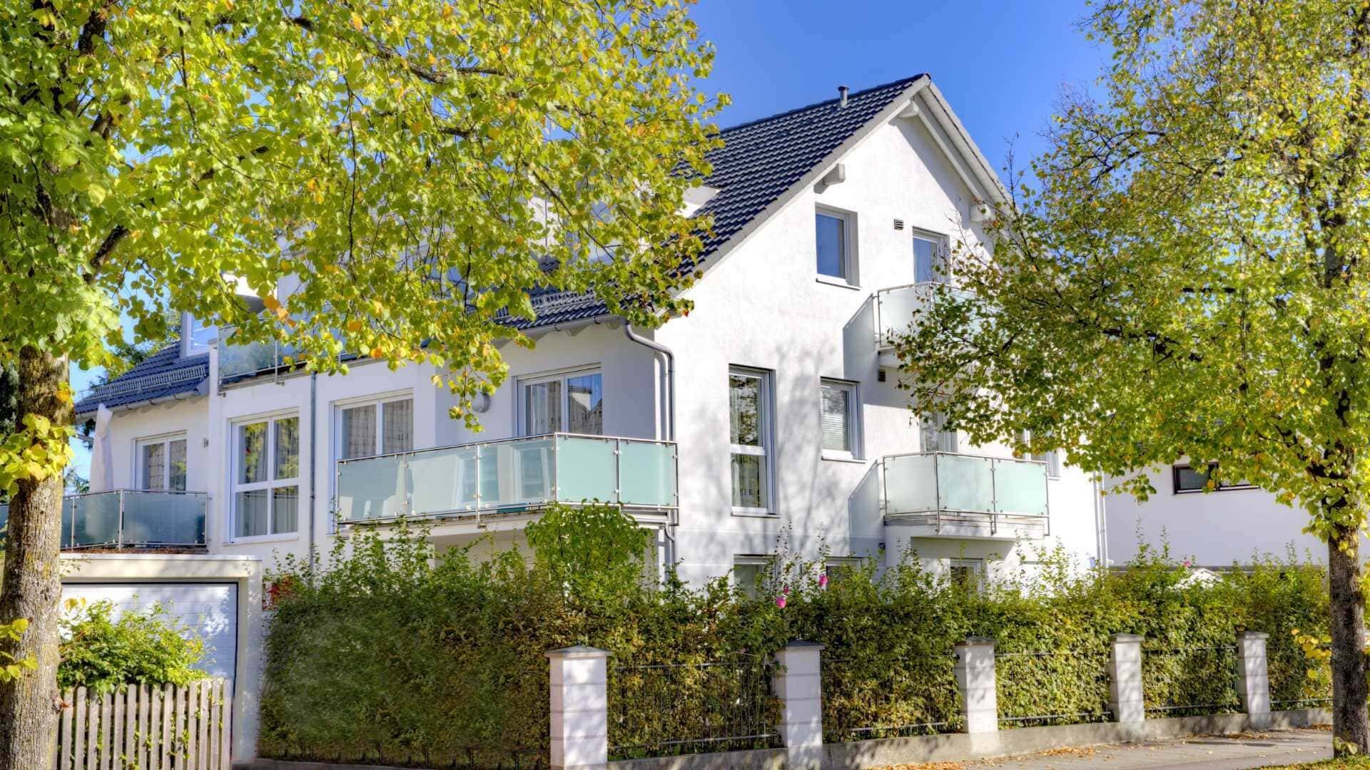 Weißes Wohnhaus mit Balkonen zwischen herbstlich gefärbten Bäumen – Symbolbild zu Immobilienpreisen in Forstenried