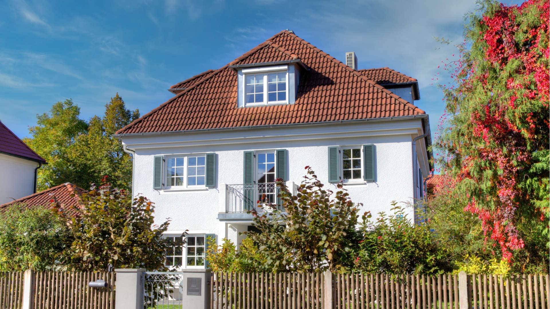 Weißes Haus mit rotem Ziegeldach und herbstlich rankendem Wein am Zaun – Symbolbild zu Immobilienpreisen in Harlaching