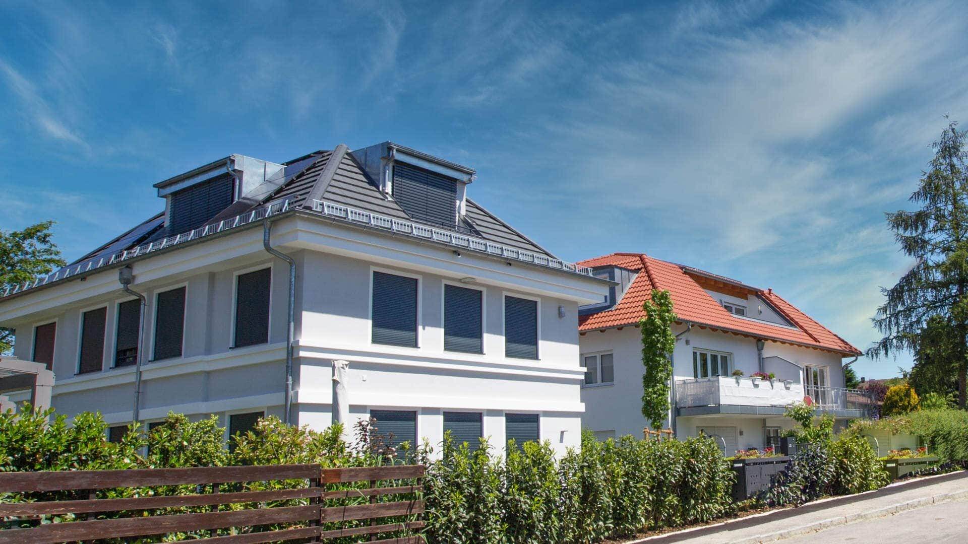 Weißes Wohnhaus mit Gaube und dunklen Fensterläden hinter Hecke in München-Laim