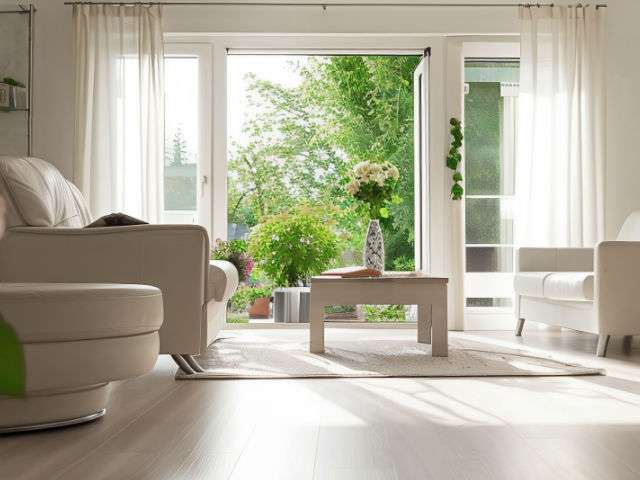 Helles Wohnzimmer mit weißen Sofas und geöffneter Terrassentür zum Garten – Symbolbild zu Immobilienpreisen in Unterhaching