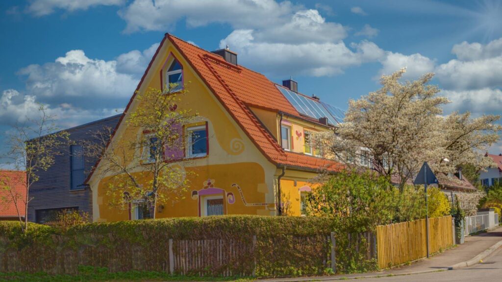 Gelbes Einfamilienhaus mit orangefarbenem Ziegeldach und Hecke – Symbolbild zu Hinweisen zur Beurkundung beim Immobilienverkauf