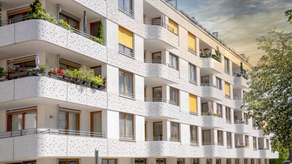 Weißes Mehrfamilienhaus mit Balkonen und gelben Markisen – Symbolbild zum Immobilienverkauf mit Immobilienmakler in München