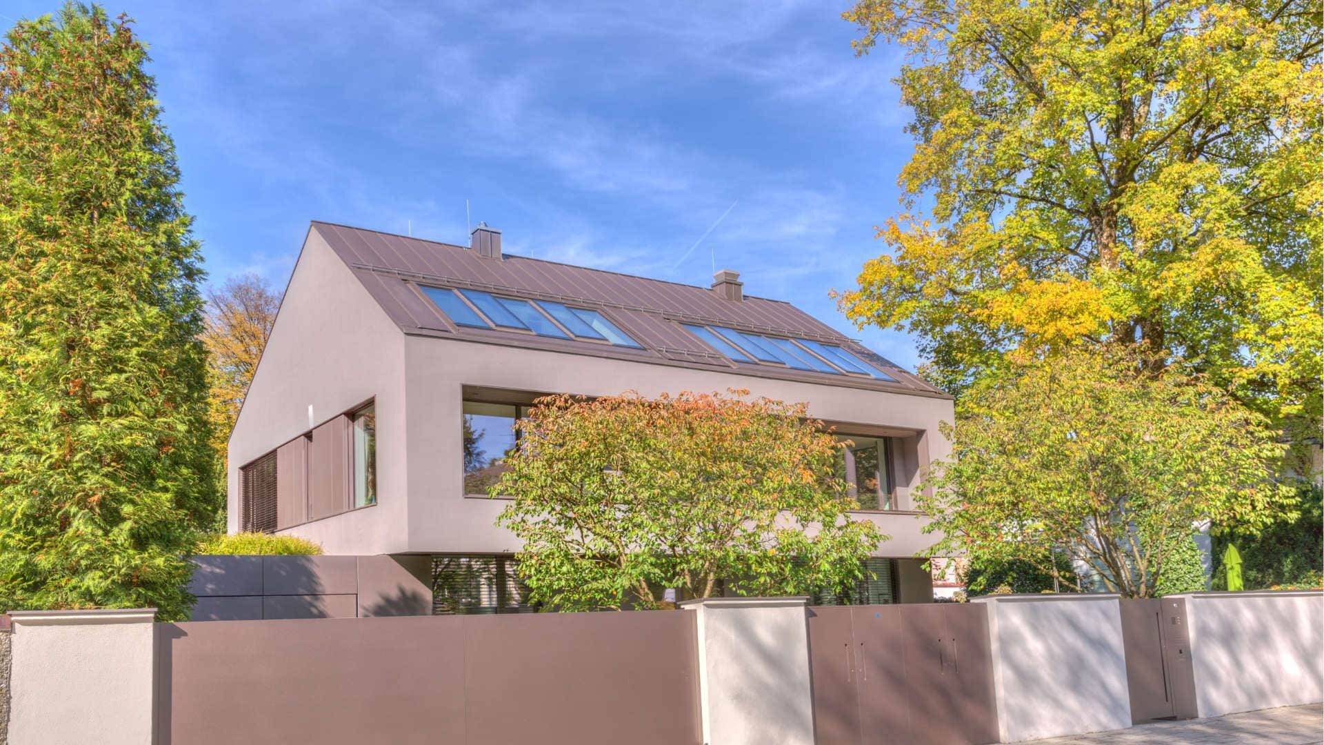 Modernes graues Flachdachhaus mit Solaranlage und herbstlichen Bäumen – Symbolbild zum Immobilienverkauf bei Scheidung
