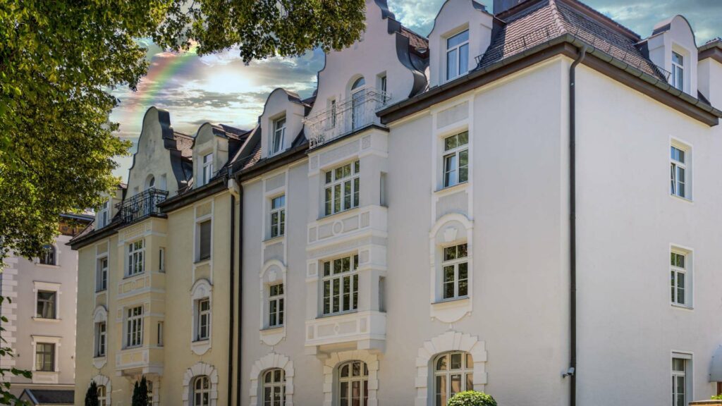 Altbauzeile mit hellen Fassaden und Gauben unter Baumkronen in München