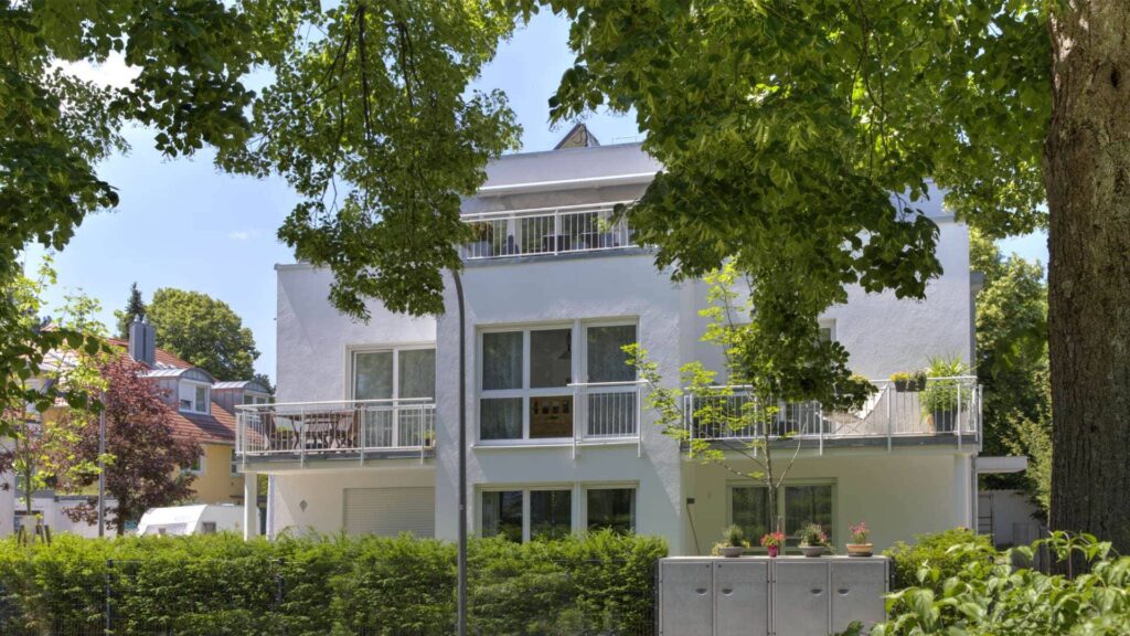 Weißes modernes Gebäude mit rundem Erker, großen Fenstern und Hecke – Symbolbild zum Kaufpreis im Kaufvertrag