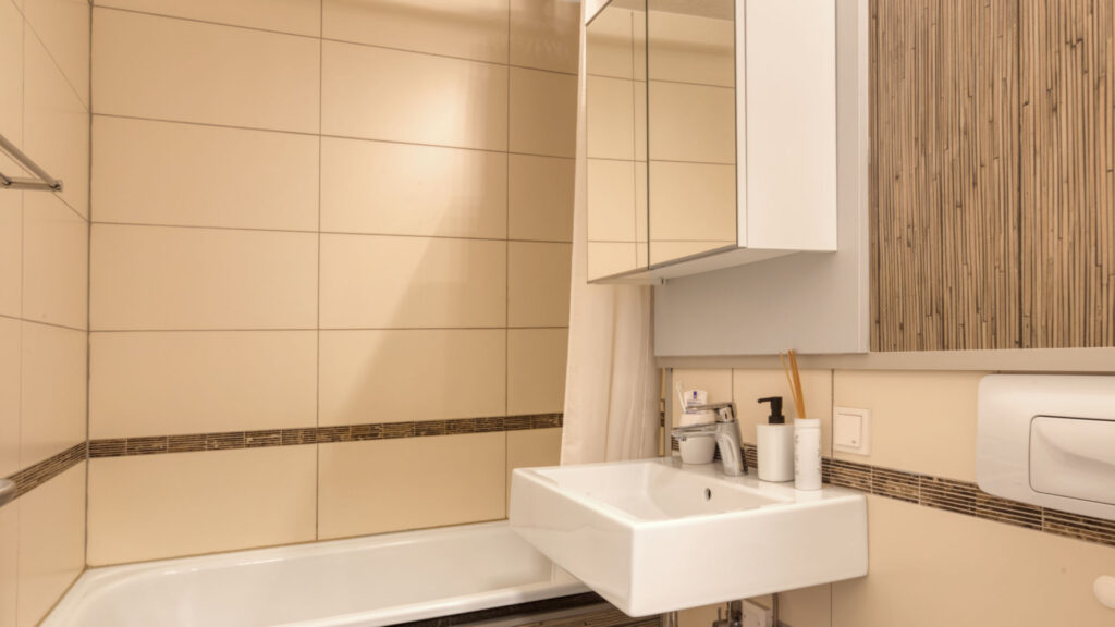 Bathroom of the Laimer apartment with beige tiles, sink and mirror cabinet above the bathtub