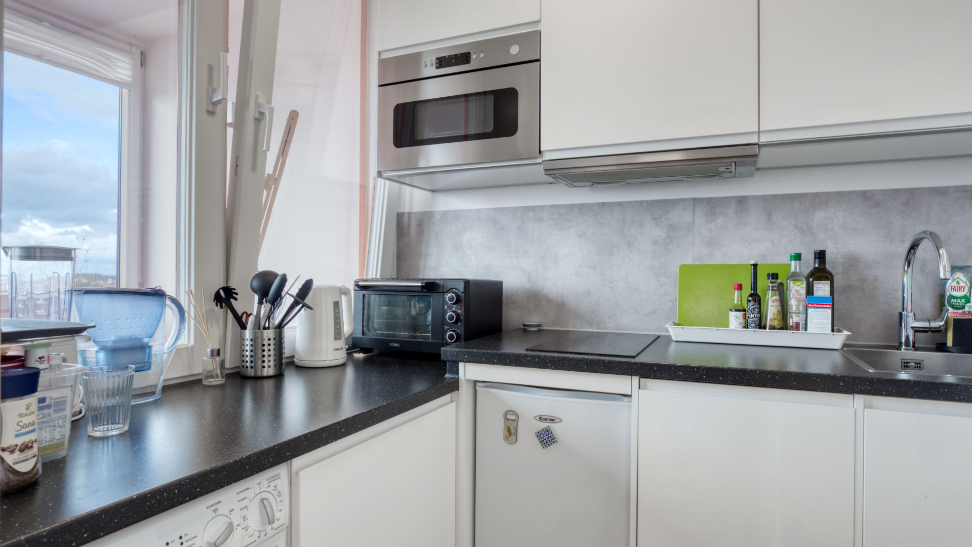 Weiße Küchenzeile der Laimer Wohnung mit Arbeitsplatte, Fenster und Blick nach draußen
