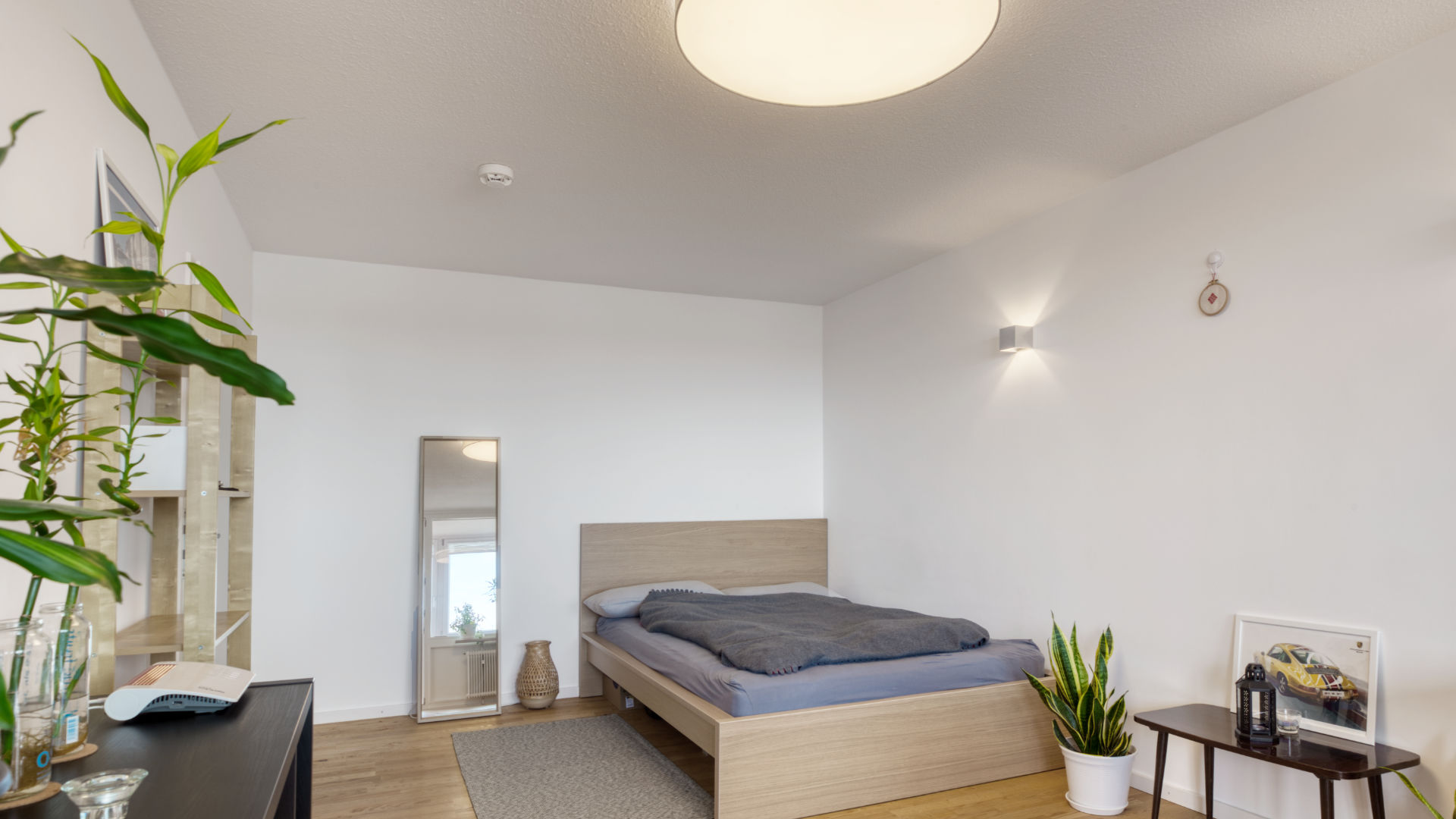 Möbliertes Schlafzimmer der Laimer Wohnung mit Holzbett, Grünpflanzen und Wandspiegel