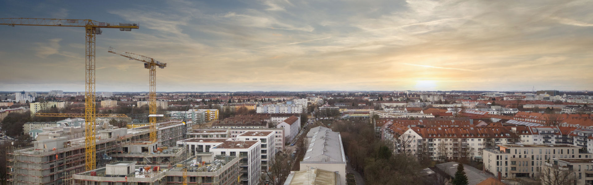 Breiter Panoramablick über München mit Baukränen und Häuserzeilen bei Abendlicht