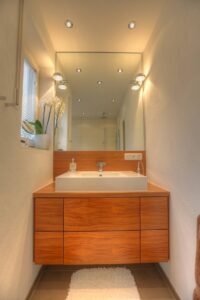 Modernes Badezimmer des Lerchenauer Hauses mit Holzwaschtisch, großem Spiegel und Aufsatzwaschbecken