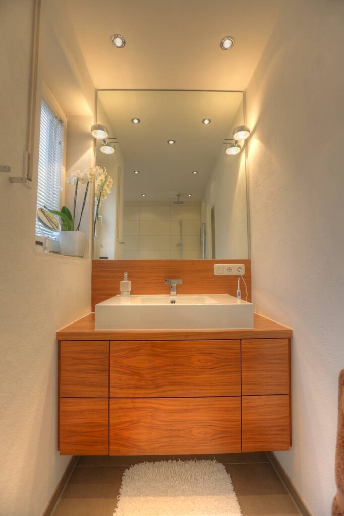 Modernes Badezimmer des Lerchenauer Hauses mit Holzwaschtisch, großem Spiegel und Aufsatzwaschbecken