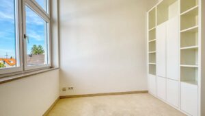Leeres Zimmer im Dachgeschoss des Lerchenauer Hauses mit weißem Einbauschrank und Fenster