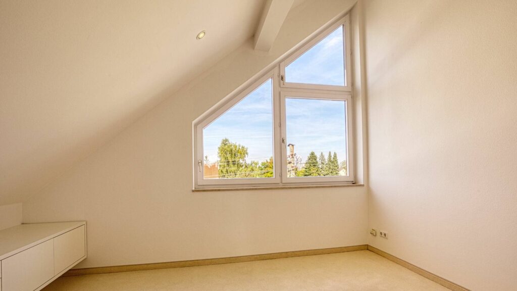 Leeres Dachgeschosszimmer des Lerchenauer Hauses mit Dachschräge und Blick über die Nachbarschaft